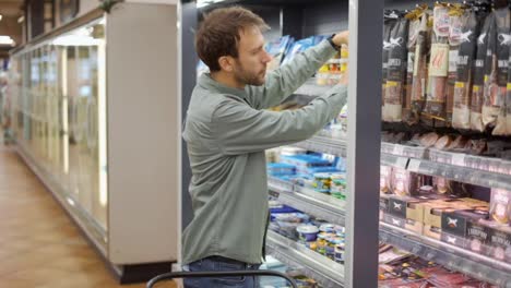 Hombre-Con-Camisa-Caminando-Con-Un-Carrito-Por-El-Supermercado-Eligiendo-Y-Llevando-Alimentos-En-El-Refrigerador