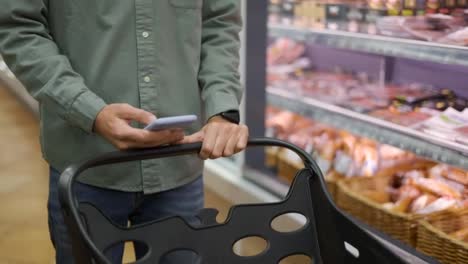 Mann-Benutzt-Mobiltelefon-Beim-Einkaufen-Im-Supermarkt,-Trolley-Einkaufszentrum,-Lebensmittelladen