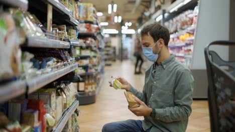 Man-in-mask-takes-groceries-from-the-food-shelf.-Shopper-choosing-goods-at-grocery-store