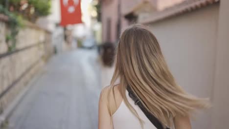 Woman-walks-along-narrow-turkish-street,-looks-back-over-her-shoulder