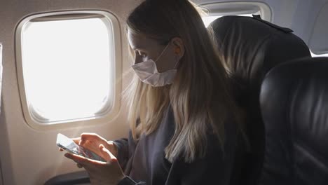 Frau-Trägt-Eine-Schutzmaske-Und-Spielt-Im-Flugzeug-Mit-Ihrem-Telefon