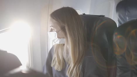 Frau-Mit-Schutzmaske-Im-Flugzeug,-Die-Zum-Fenster-Blickt