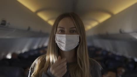 Portrait-of-a-woman-standing-in-a-seat-row-on-plane,-taking-off-mask-to-smile