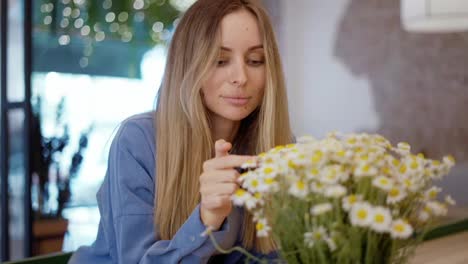 Blonde-woman-looking-and-touching-beautiful-bouquet-of-chamomile-flowers