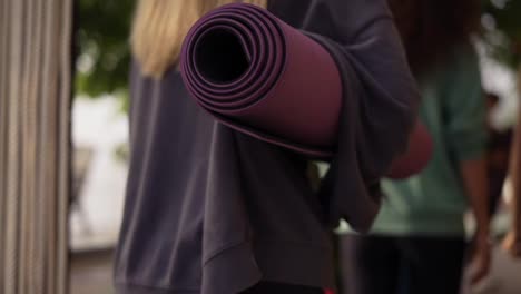 Rear-view-women-go-together-for-exercise-holding-mats-for-yoga,-Close-Up