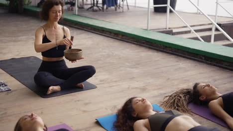 Woman-holding-singing-bowls-in-her-hands-lead-yoga-class-outdoors