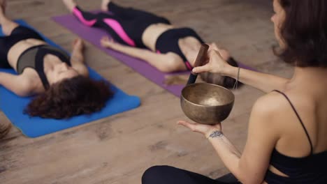 Mujer-Usando-Cuencos-Cantores-Durante-La-Meditación,-Dirige-Una-Clase-De-Yoga-Al-Aire-Libre