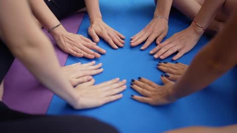 Women-after-yoga-training-collecting-their-hands-on-a-mat,-closeup