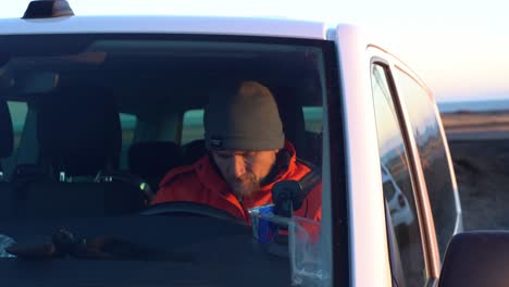 Caucasian-Man-Writes-on-his-Cellphone-inside-a-Car,-Diamond-Beach-Iceland-Winter