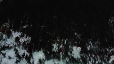 Aerial-top-view-foamy-waves-break-on-dark-rocks-near-beach.-Sea-waves-on-the-dangerous-stones-aerial-view-drone-4k-shot.-Rolling