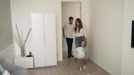 Young-family-in-the-hotel-room.-A-child-with-parents-and-luggage-enters-the-hotel-room.-Little-girl-holding-a-big-plastic-globus
