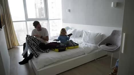 Young-family-making-fun-while-packing-for-holiday.-Caucasian-man,-woman-and-child-in-bedroom.-Little-kid-is-sitting-in-the-small