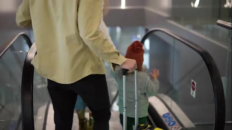 Rare-view-of-caucasian-family-with-yellow-stylish-suitcase-going-down-by-the-escalator-with-their-pretty-daughter-hold-by