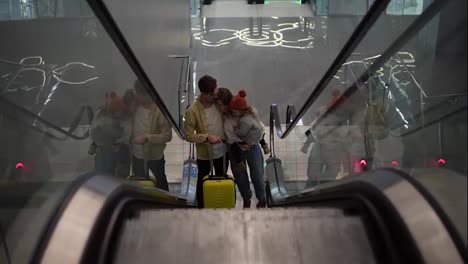 Happy,-young-family-with-yellow-suitcase-going-up-by-the-escalator-from-the-airport-hall.-Smiling-mother-holds-pretty-daughter