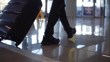 Close-up,-cropped-shot-of-man-legs-with-the-black-baggage-walking-to-the-airport-terminal.-Slow-motion