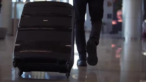 Close-up,-cropped-shot-of-man-legs-with-the-black-baggage-walking-to-the-airport-terminal.-Slow-motion.-Rare-view