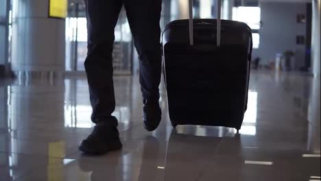 Close-up,-cropped-shot-of-man-legs-with-the-black-baggage-walking-to-the-airport-terminal.-Slow-motion.-Front-view