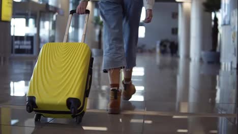 Stylish-woman-walk-with-trolley-yellow-case-by-empty-airport,-low-half-view-of-slender-female-legs-and-medium-wheeled-bag