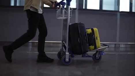 Unrecognizable-male-passenger-with-luggage-trolley-in-the-international-airport.-Walking-in-the-hurry,-side-view