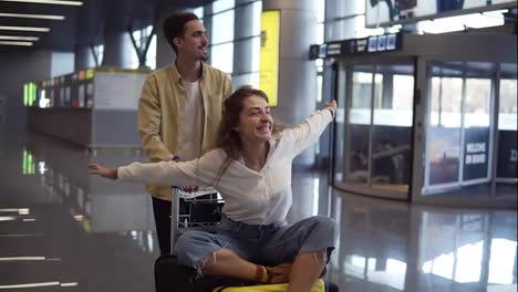 Romantic-couple-in-airport.-Attractive-young-woman-and-handsome-man-with-suitcases-are-ready-for-traveling.-Having-fun-on