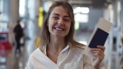 Portrait-of-happy,-beautiful-american-woman-showing-passport-with-flight-tickets-and-waving-it.-Looking-and-smiling-to-the