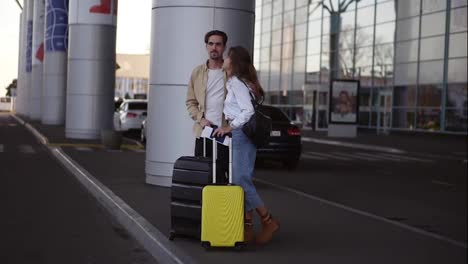 Stylish,-young-couple-with-luggage-standing-on-airport-parking-with-their-suitcases.-Waiting-for-car-after-arrival