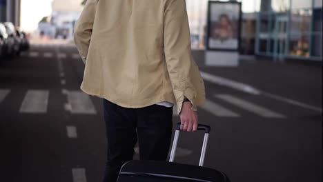 Close-up,-cropped-shot-of-married-man-with-the-black-baggage-walking-to-the-outside-airport-terminal-by-road.-Slow-motion.-Rare