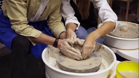 Dirty-couple's-hands-close-up-.-Romantic-couple-in-love-working-together-on-potter-wheel-and-sculpting-clay-pot.-Woman-pouring-water,-working-together-in-craft-studio-workshop.-No-faces