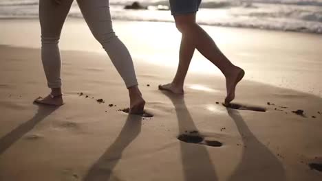 Relaxful-couple-walking-barefoot-on-the-beach.They-are-spending-time-together,-leaving-footprints-on-wet-sand,-holding-hands.-Mild-sunset-on-the-background.-Rare-view