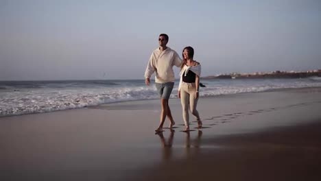 Couple-romantic-walk-on-beach,-lovers-walking-barefoot-on-sand.-Summer,-couple-in-love,-an-exotic-vacation,-wind-waving-female-hair,-background-sand-and-water,-sunny-weather