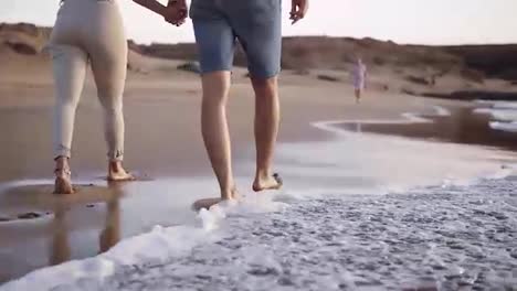 Unrecognizable-young-couple-stepping-together-at-the-golden-sand-at-sea-beach.-Male-and-female-legs-walking-near-ocean.-Bare