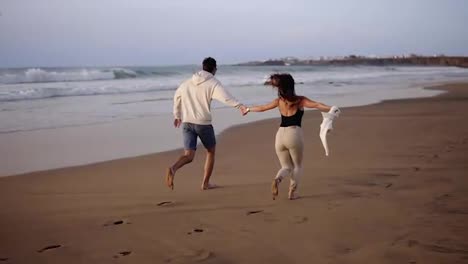 Couple-enjoy-summer-vacation-on-the-large-beach,-enjoy-life-and-running-in-scenery-slow-motion-video-on-background-ocean-landscape.-Young-couple-running-into-tropical-ocean-rare-view