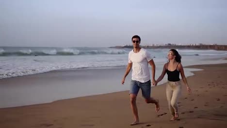 Couple-enjoy-summer-vacation-on-the-large-beach,-enjoy-life-and-running-in-scenery-slow-motion-video-on-background-ocean-landscape.-Young-couple-running-into-tropical-ocean,-happy-smile