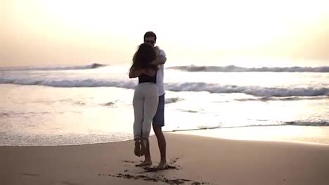 Young-beautiful-couple-walking-by-the-sea.-Boy-and-girl.-They-are-happy.-Tall-guy-takes-the-tiny-girl-in-his-arms-and-turns-her-around.-Silhouettes-on-an-ocean-background