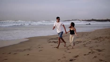 Perfect-scene.-Couple-enjoy-summer-vacation-on-the-large-beach,-enjoy-life-and-running-in-scenery-slow-motion-video-on-background-ocean-landscape.-Young-couple-running-into-tropical-ocean,-happy-smile