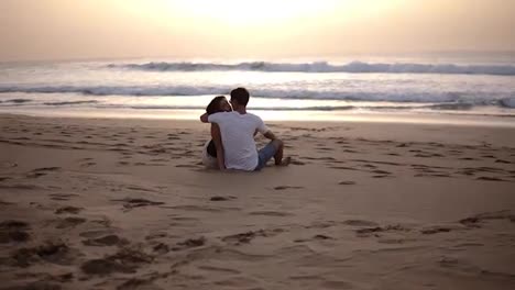 Ein-Paar-Sitzt-Im-Sand-Am-Strand,-Blickt-Auf-Das-Meer-Und-Küsst-Sich-Im-Sonnenuntergang.-Sinnliche-Szene-Von-Zwei-Liebenden-Menschen,-Die-Allein-Vor-Dem-Meer-Sitzen