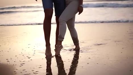 Couple-of-lovers-man-and-woman-paint-with-their-feet-on-the-wet-sand-heart.-Cropped-footage-of-loving-couple-on-the-sea-coast.-Slow-motion