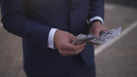 Solid-rich-businessman-on-the-street-holding-bundle-of-american-money-in-his-hands,-counting-it.-Wealthy-male-counts-hundred