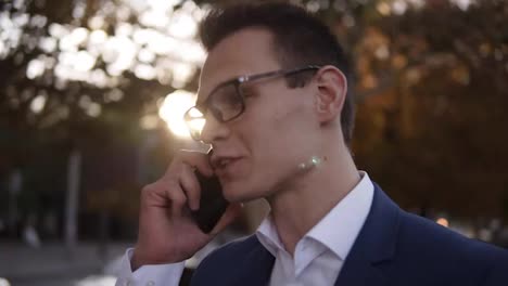 Caucasian-businessman-in-stylish-glasses-talking-on-the-mobile-phone-on-streets-of-business-district.-Young-confident-man-using