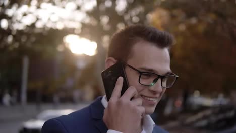 Portrait-of-businessman-in-stylish-glasses-talking-on-the-mobile-phone-on-streets-of-business-district.-Young-smiling-man-using
