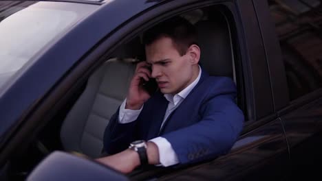 Handsome-man-sitting-in-the-car-on-a-driver's-seat,-holding-hand-on-the-car-door.-Businessman-talking-while-sitting-in-a-car