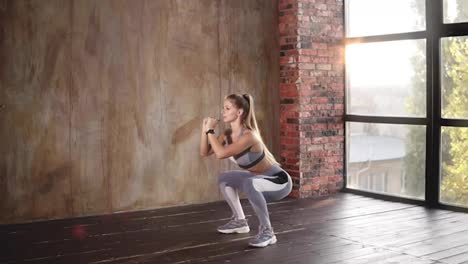 A-young-athlete-professionally-performs-squats.-Muscular-young-woman-in-grey-sportswear-doing-physical-exercises.-A-woman-shows