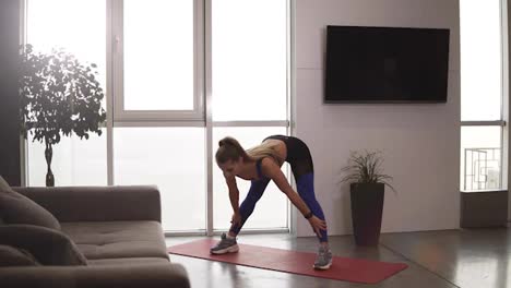 Slender-caucasian-lady-is-doing-sports-at-home-stretching-body,-arms-and-legs-leaning-to-the-floor-enjoying-activity-and-healthy-lifestyle.-Sport-and-millennials-concept