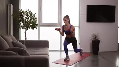 Strong-fitness-woman-lifting-dumbbells-while-doing-lunges,-enjoying-proper-breathing-during-training.-Pretty-athletic-female-making-sports-exercise-at-home-on-a-mat