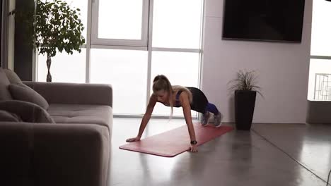 Healthy-young-woman-in-sportswear-doing-push-ups-on-fitness-mat-in-her-bright-living-room.-Young-longhaired-female-exercising-at-home.-Slow-motion
