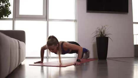 Healthy-young-woman-in-sportswear-doing-push-ups-on-fitness-mat-in-her-bright-living-room.-Young-longhaired-female-exercising-at-home.-Slow-motion.-Close-up