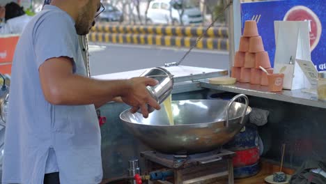 Front-view-of-a-man-taking-out-organic-A2-milk-from-a-steel-vessel-to-heat-it-on-a-pan-in-his-shop