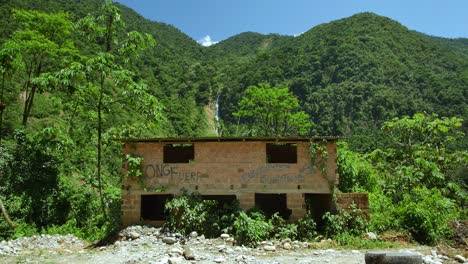 Shack-by-Bolivian-forest,-hills,-waterfall,-sky-in-background