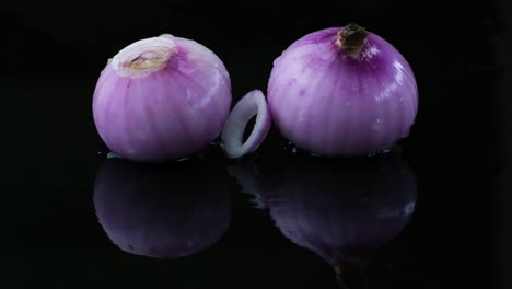 Water-drops-and-rings-falling-on-raw-red-onions,-studio-shot
