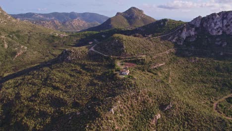 Wide-shot-of-small-house-surround-by-mountains-at-Mallorca,-Balearic-Islands,-aerial